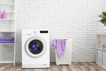 Modern washing machine near brick wall in laundry room interior, space for text