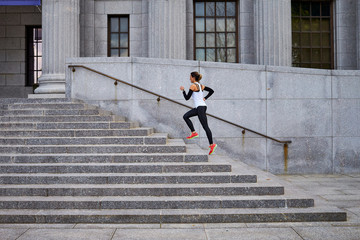 Female jogger running up steps of city building, Boston, Massachusetts, USA