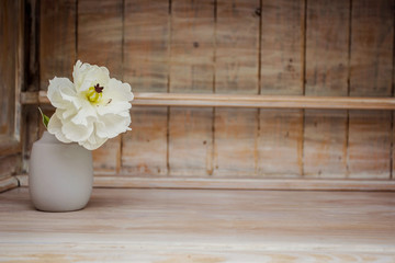 Soft home decor, vase with white small flower on a white vintage wooden wall background and on a wooden shelf. Interior.