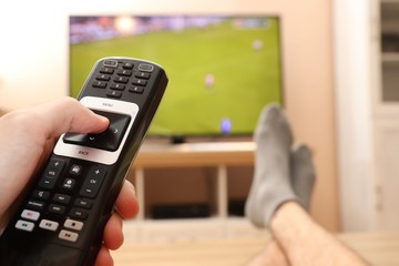 TV remote control in hand. Feet on the table. Watching football.