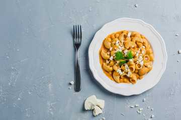 pasta Pipa the rigat with a sauce of chickpeas and tomatoes, sprinkled with feta cheese and cilantro on a white plate on a light grey background high angle