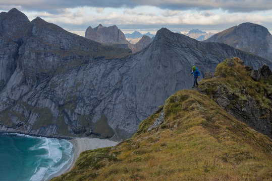 Female hiker walking along narrow ridge near Storskiva mountain peak with Brunes beach in distance