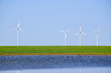 White windmills over a field of young green wheat and a lake covered with ripples.