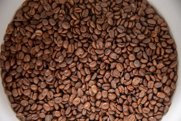 Coffee seeds in a big ceramic mug on a table background. Heap of coffee beans in cup.
