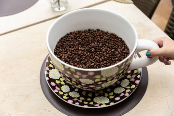 Coffee seeds in a big ceramic mug on a table background. Heap of coffee beans in cup.