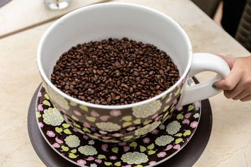 Coffee seeds in a big ceramic mug on a table background. Heap of coffee beans in cup.