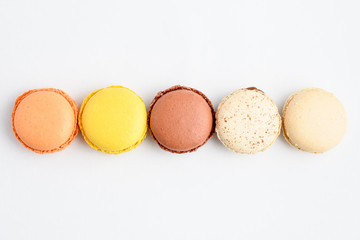 Close up of a row of five sweet French macarons with different aromas, isolated on white, flavours of orange,  lemon, caramel, chocolate, coconut and vanilla, pastel colors