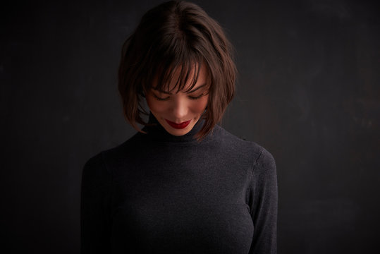 Young Woman Studio Portrait While Standing At Dark Background And Looking Down