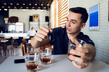 Young man drunk at bar drinking alcohol whiskey holding car keys drink and drive safety concept