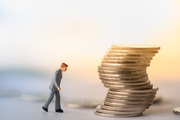 Business, Risk Management, Money and Planning Concept. Close up of businessman miniature figure walking on ground to unstable stack of coins.