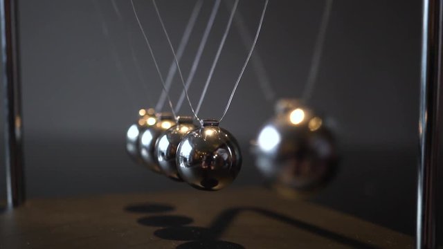 Close-up video of metal Newton cradle swining on gray background as representation of momentum concept