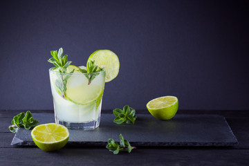 Cocktail mojito and mint on black background. Refreshing cocktail with lime and fresh mint on slate board. Summer drink with citrus and ice. Copy space