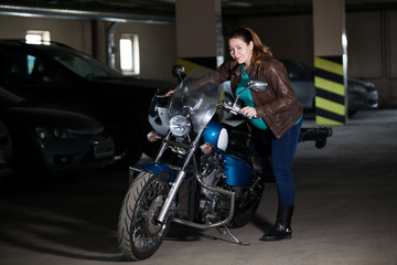 Plakat Full-figured woman getting on bike in dark garage, concept of pregnant with motorcycle
