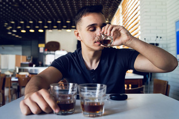 Young man drunk at pub cafe bar holding glass of alcohol drinking whiskey brandy