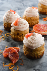 Homemade healthy sugar free sweets. Muffins with cream cheese and blood orange icing on dark background