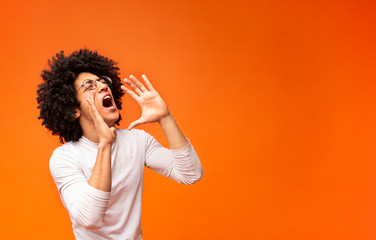 Young african-american man yelling on orange background