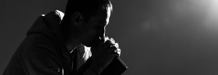 Religious young man praying to God on dark background, black and white effect