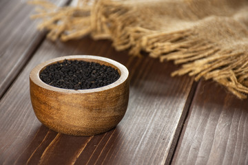 Fototapeta na wymiar Lot of whole black cumin seeds with wooden bowl and jute cloth on brown wood