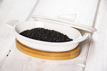 Lot of whole black cumin seeds in a ceramic stewpan on white wood