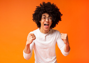 Excited african-american man shakes clenched fists at studio