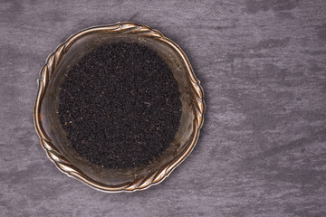 Lot of whole black cumin seeds in old iron bowl flatlay on grey stone