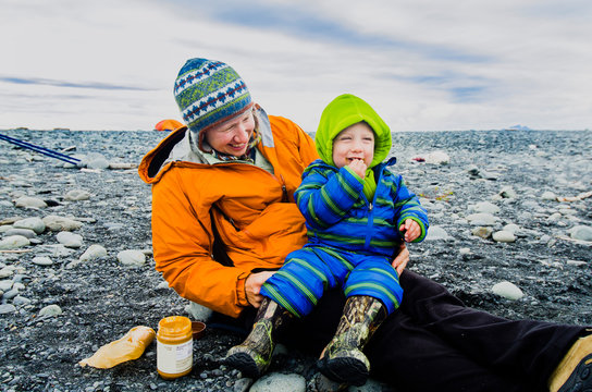 Mom and two year old son enjoy a peanut butter and cracker snack on the rocky beach next to Bear Lake in Kenai Fjords National Park, Alaska.