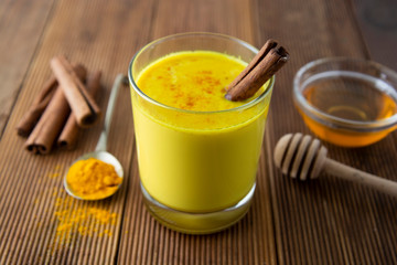 Turmeric Golden Milk. Healthy drink made with turmeric honey and cinnamon. Remedy for many diseases. Rustic wooden background.