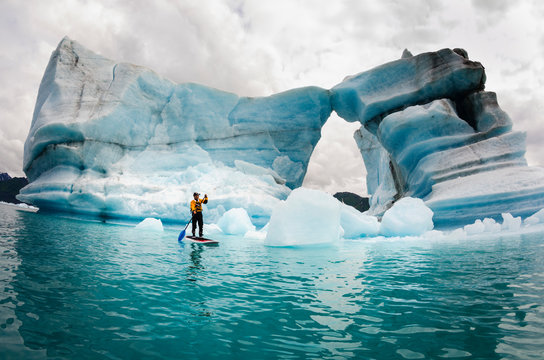 Man on stand up paddle board against iceberg