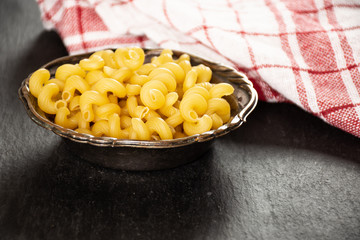 Lot of whole pasta cavatappi with a tea towel in old iron bowl on grey stone