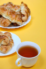 croissants on a white plate with a Cup of tea on a yellow background