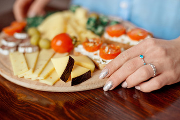 Close-up photo cheese plate - woman's hands cutting different kinds of cheeses in counter at kitchen home interior.