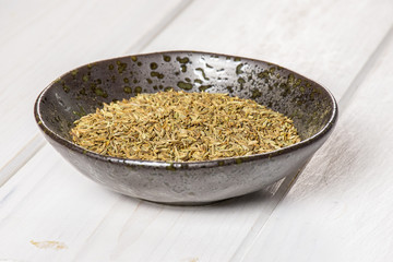 Lot of whole roman caraway seeds in a grey ceramic bowl on white wood