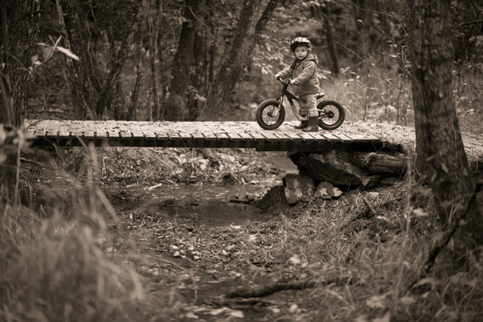 Baby boy with bicycle on footbridge in forest, Rancho Santa Elena, Hidalgo, Mexico