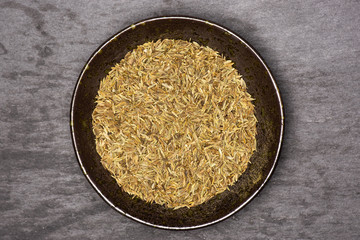 Lot of whole roman caraway seeds in a grey ceramic bowl flatlay on grey stone