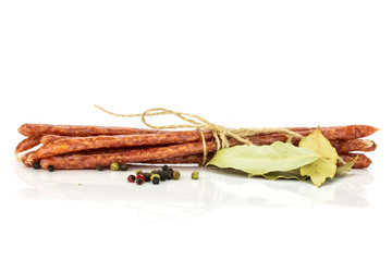 Lot of whole spicy salami stick tyrolini tied by jute with bay leaf and black pepper isolated on...