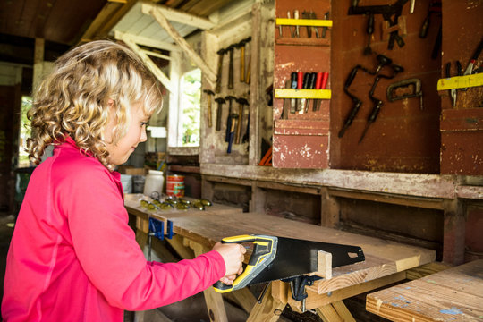 A Young Girl Cutting A Plank Wood With A Saw At Camp Woodshop