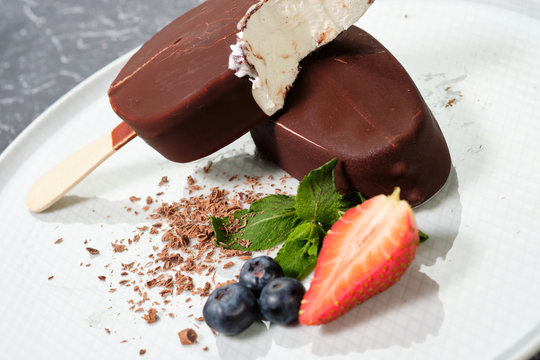 chocolate butter ice cream popsicles on the white plate with fresh summer berries, strawberries, blueberries