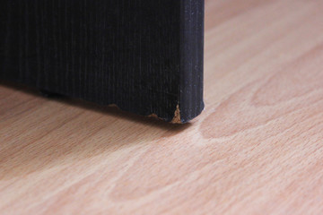 Old damaged edge of threadbare table on wooden floor background. Interior detail of broken worn out...
