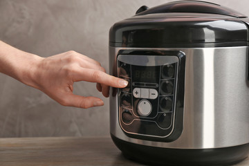 Woman turning on modern electric multi cooker on grey background, closeup