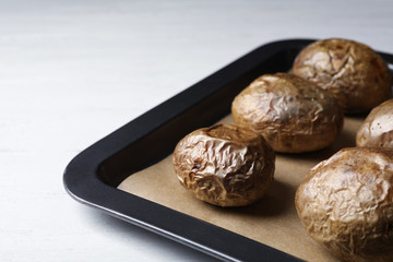 Tray with baked jacket potatoes on table, closeup