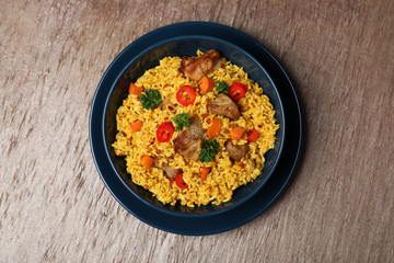 Plate with rice pilaf and meat on wooden background, top view