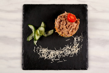 Meat salad with cucumber, tomato and cheese on a black tray.