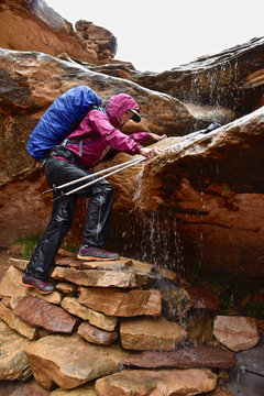 Female hiker climbing slippery rock with flowing water