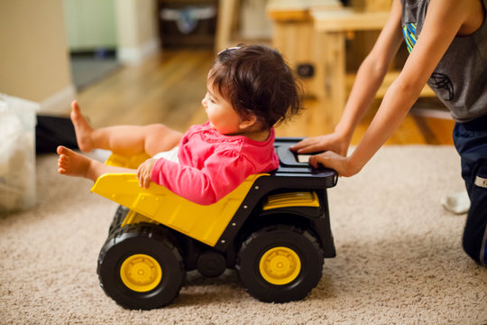 A Japanese American one year old baby girl is pushed in a toy dump truck by her older brother.