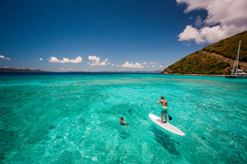 BRITISH VIRGIN ISLANDS, CARIBBEAN. A woman paddles a stand-up paddle board in clear teal Caribbean Island water.