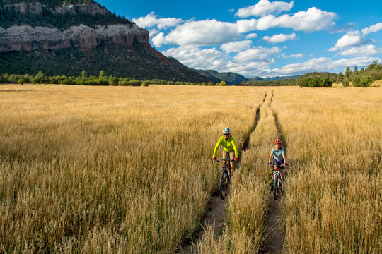 Woman with daughter riding mountain bikes through a grass field in Falls Creek