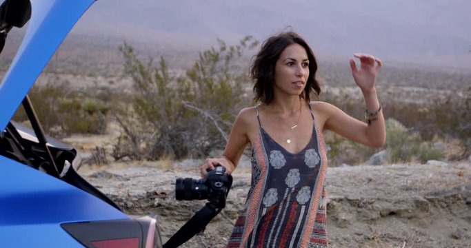 Stylish female photographer grabs camera out of truck of car in desert - slow motion