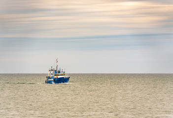 Small single fishing boat at the open sea with scenic sky.
