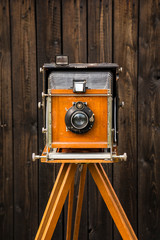 An old large format camera on a wooden tripod.