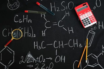 Fototapeta na wymiar Laboratory glassware and school supplies on blackboard with chemical formulas, flat lay